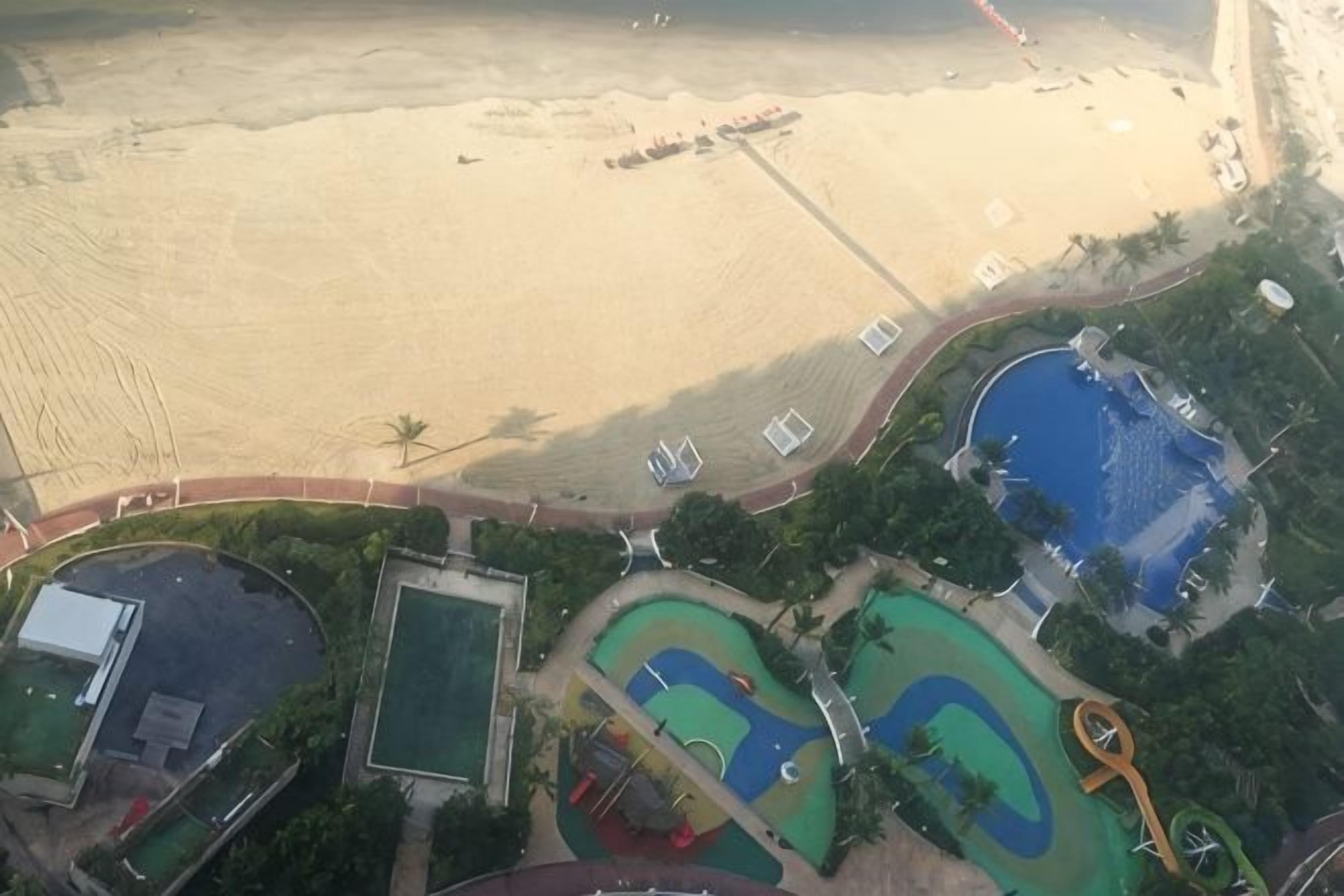 Vista aérea de un resort con playa, piscinas y un parque infantil.