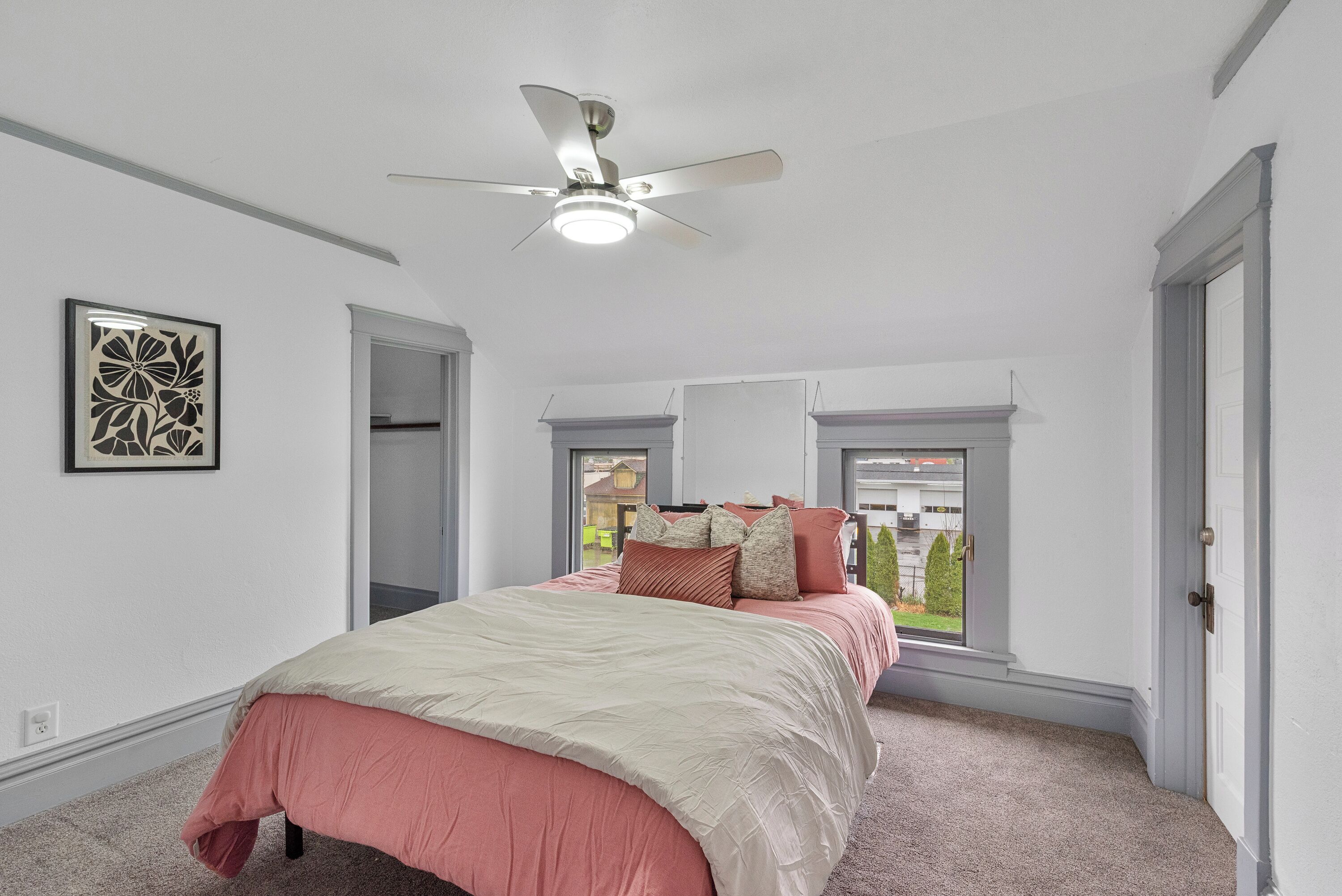 A bedroom with a bed, a ceiling fan, a window, and a door.