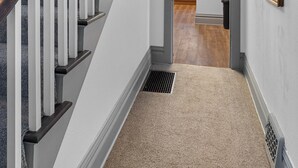 Una escalera con barandilla de madera y alfombra color beige que conduce a una zona de cocina.