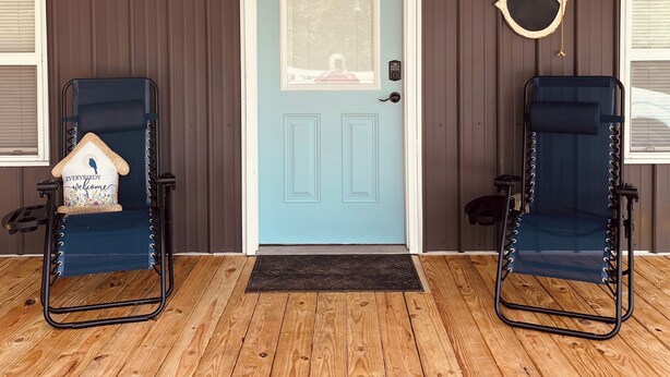 A covered porch with a blue door, two blue chairs, and a heart-shaped decoration on the wall. - The Wren’s Nest (LaFollette)