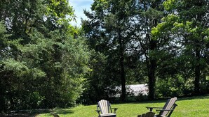 A wooden picnic table with four Adirondack chairs in a grassy outdoor area. - The Wren’s Nest (LaFollette)