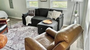 A living room with a sofa, a coffee table, a leather armchair, a floor lamp, and a rug. - The Wren’s Nest (LaFollette)