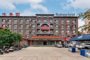 Een meerhoog hotel met een opvallende ingang, een parkeerplaats met meerdere auto's en een heldere lucht.