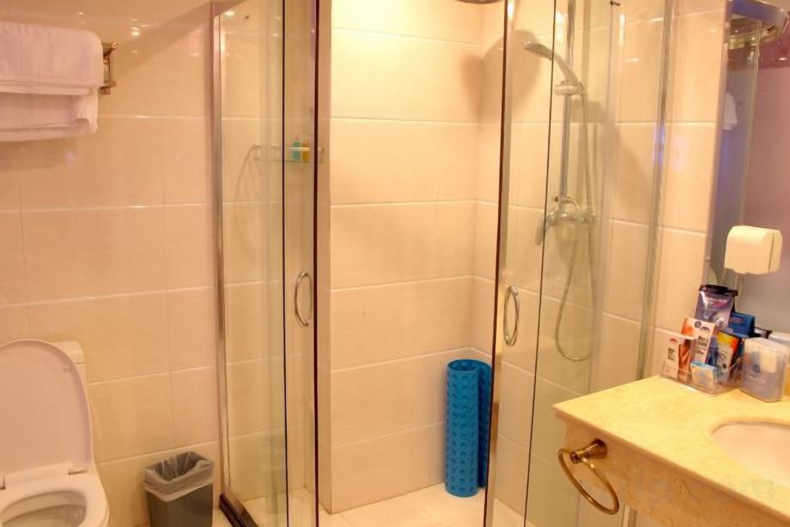 A bathroom with a glass-enclosed shower, a toilet, and a sink with toiletries.
