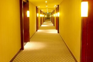 A hotel corridor with a patterned floor, wooden doors, and overhead lighting.