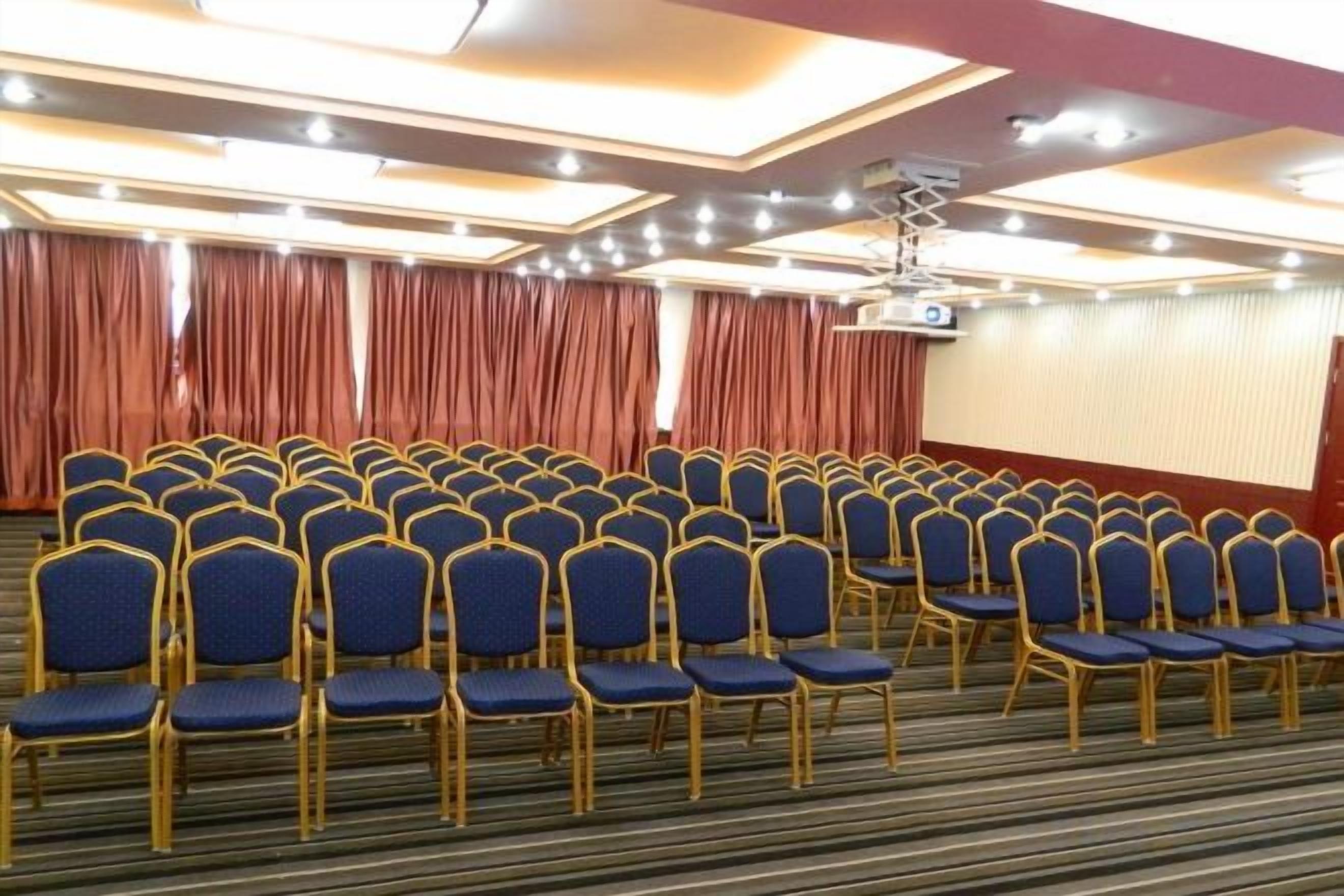 Uma sala de conferências com fileiras de cadeiras, uma tela de projetor e cortinas.