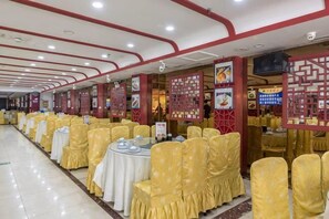 Un salón de banquetes con filas de mesas y sillas, suelo de baldosas y un diseño de techo en rojo y blanco.