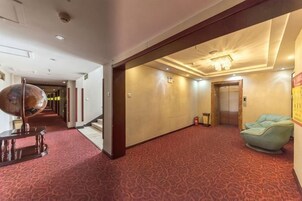 Un pasillo de hotel con alfombra roja, un sillón verde y un ascensor.