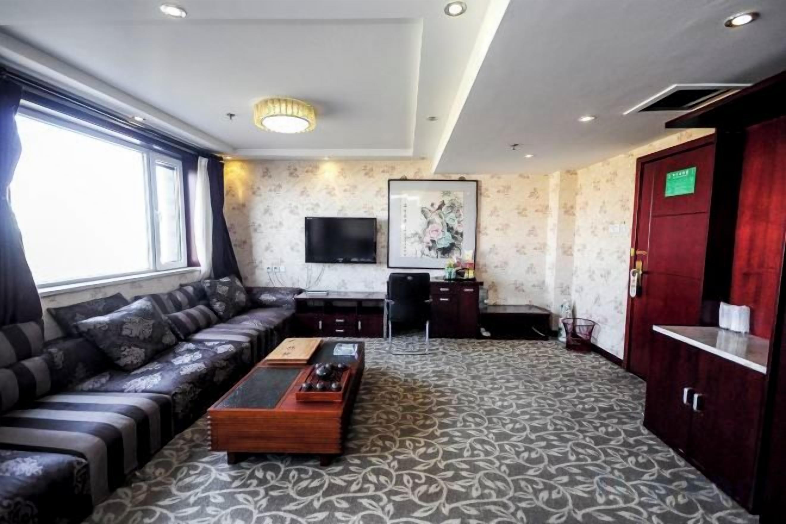 Quarto de hotel com sofá, mesa de centro, TV de tela plana e carpete estampado.