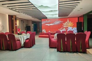 Un espace repas avec des tables rondes et des chaises rouges, un mur orné d’un tableau traditionnel et un plafond au décor original.