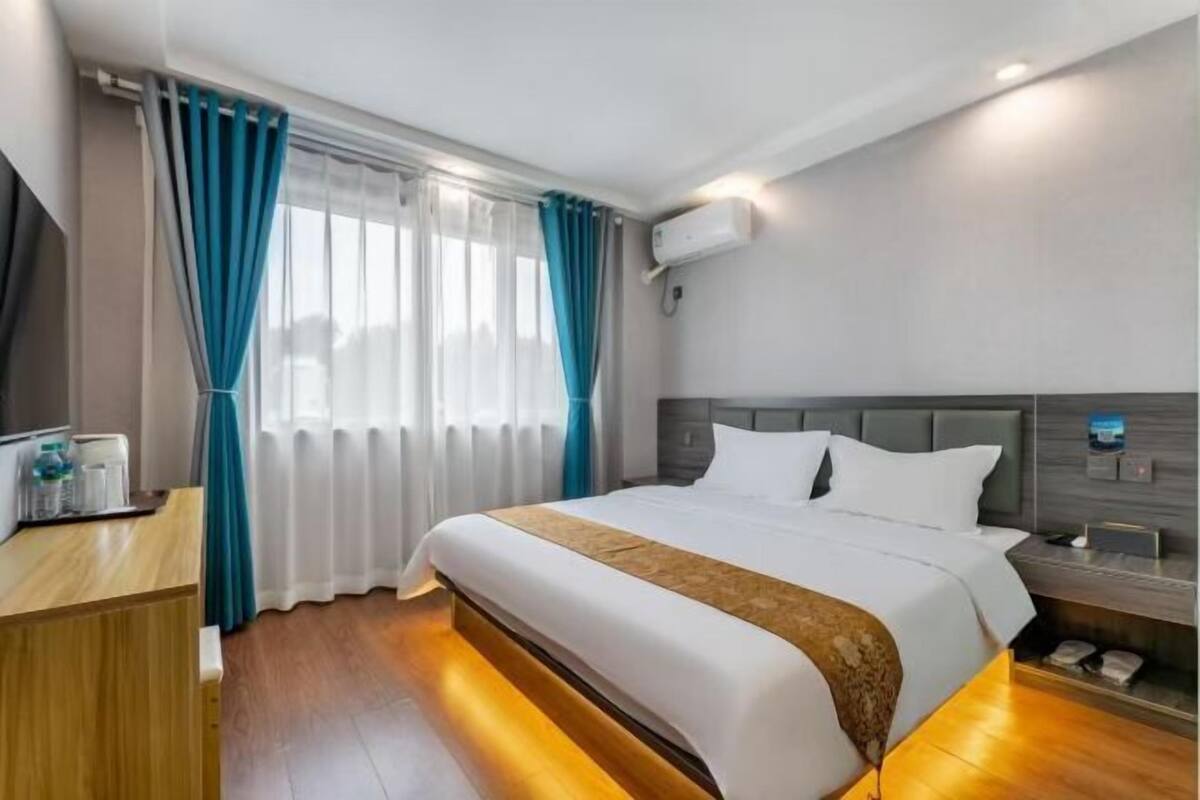 Une chambre d’hôtel comprenant un lit, une table de chevet, un bureau, une chaise, une fenêtre avec des rideaux et un appareil de climatisation.