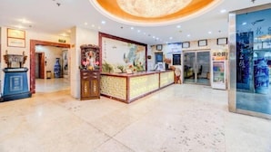 Un hall d’hôtel avec un comptoir d’accueil, un lustre et une grande fenêtre.