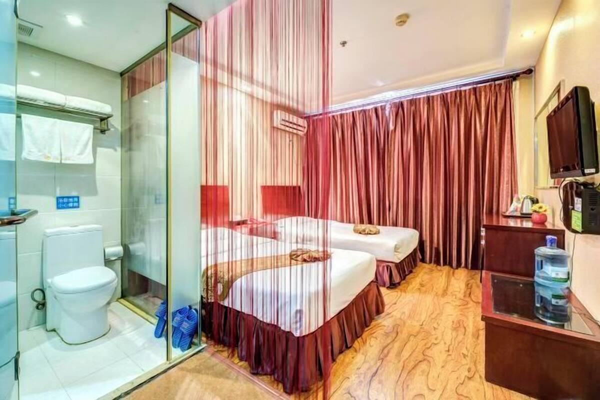 Une chambre d’hôtel dotée d’une douche en verre, de deux lits, d’un plancher en bois, d’une télévision et d’un distributeur d’eau.