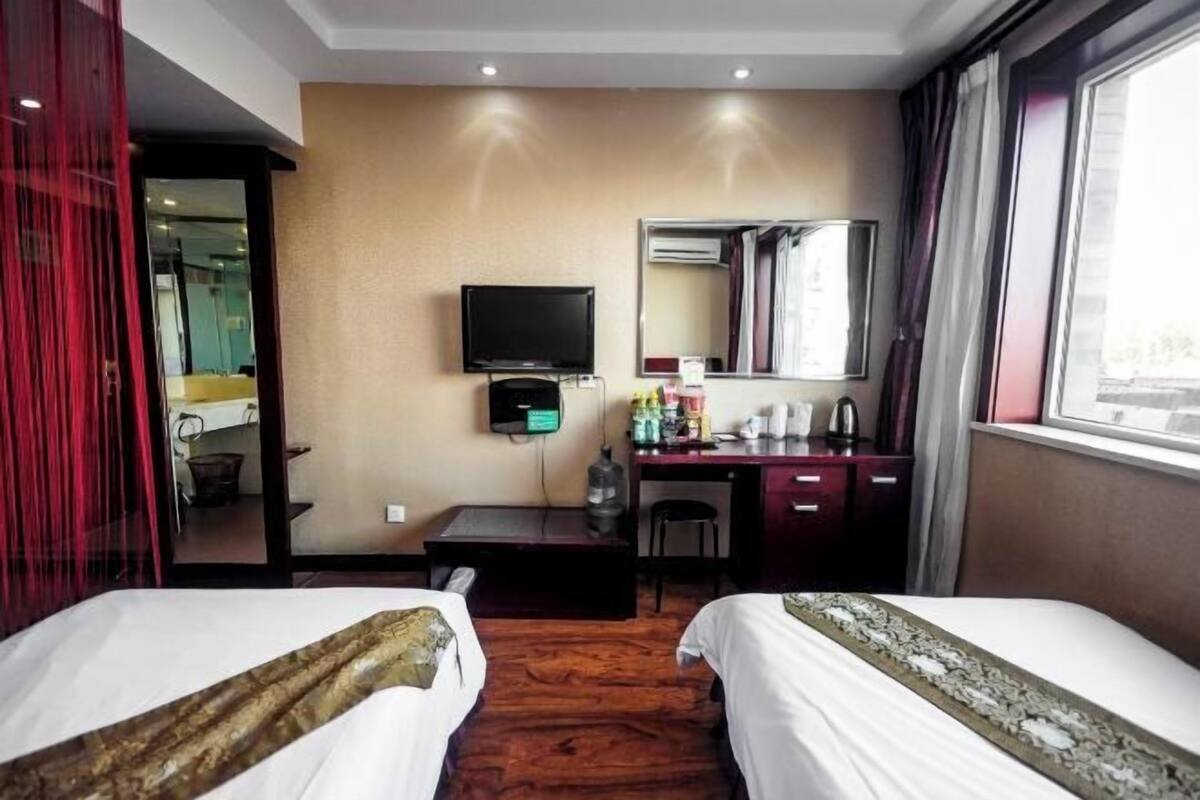 Une chambre d’hôtel avec deux lits, un bureau avec une chaise, une télévision, un miroir et une fenêtre.