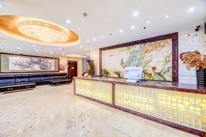 Ein Hotel-Empfangsbereich mit Marmorboden, einer Rezeption mit dekorativem Raumteiler, einem großen Wandgemälde und einer Sitzecke mit Sofas.