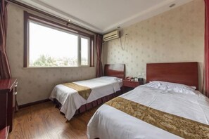 A hotel room with two single beds, a wooden floor, a window with curtains, an air conditioning unit, and a small desk with a telephone. - Baiwei Business Hotel (Qinhuangdao Railway Station) (Qinhuangdao)