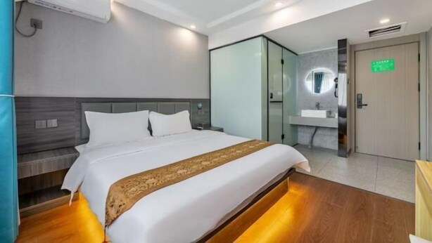 Une chambre d’hôtel moderne équipée d’un lit, d’une table de chevet, d’une armoire intégrée et d’une salle de bain avec un lavabo et un miroir.