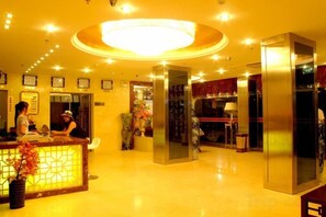 Un hall d’hôtel comprenant un comptoir d’accueil, un grand lustre et un ascenseur moderne.