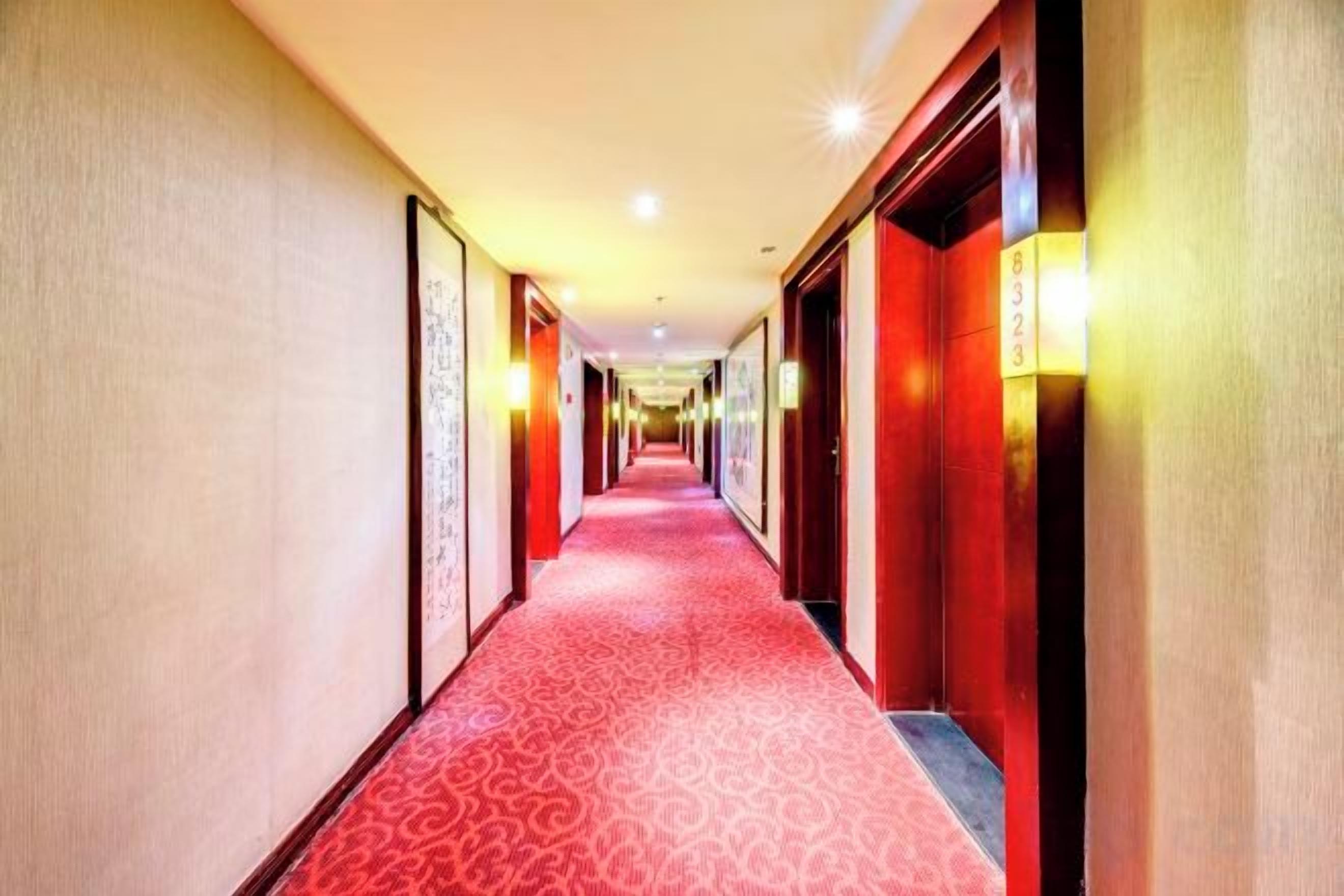 Un pasillo de hotel con alfombra roja, puertas a ambos lados e iluminación empotrada en la pared.