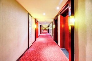 Un couloir d’hôtel avec un tapis rouge, des portes des deux côtés et des appliques murales.