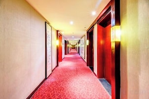 A hotel corridor with a red carpet, doors on both sides, and wall-mounted light fixtures.