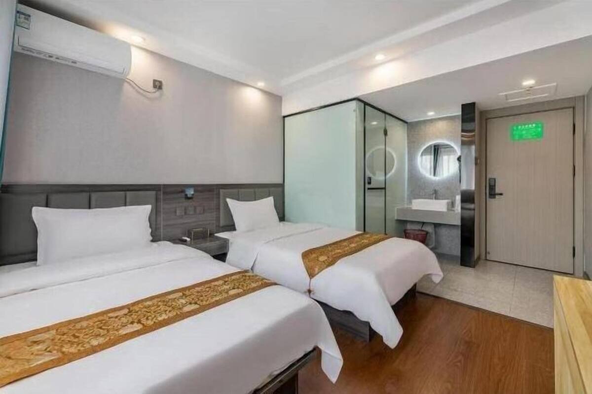 Une chambre d’hôtel avec deux lits, une salle de bain avec un miroir et une porte avec une pancarte verte.