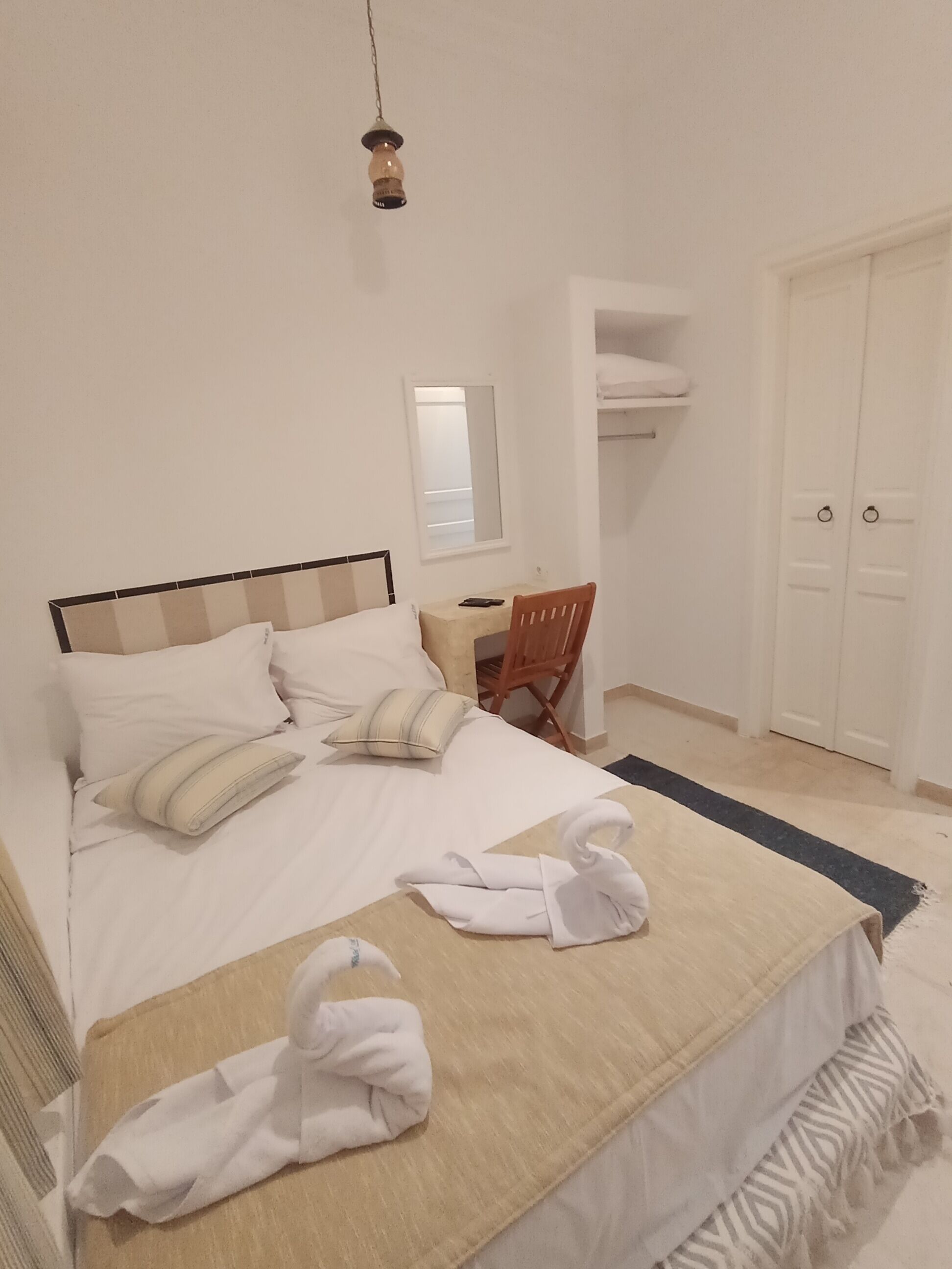 A neatly made bed with white bedding, a wooden headboard, a bedside table with a lamp, a chair, and a wardrobe.