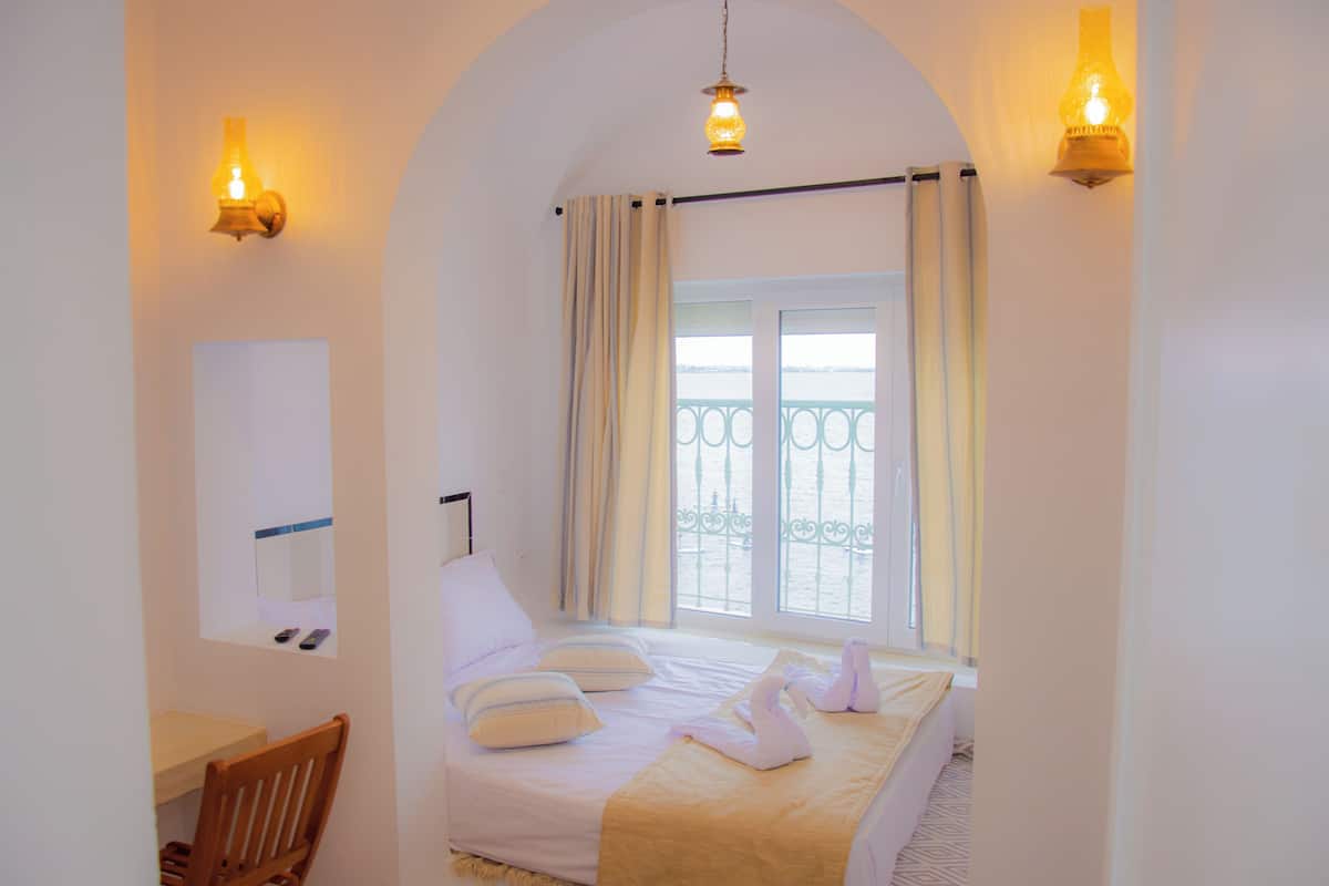 A hotel room with a bed, a desk, and a view of the sea through a balcony.