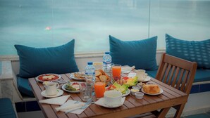 A table set with breakfast items, including plates of food, drinks, and a cup, overlooking a body of water. - Hotel Al Jazira (Mahdia)