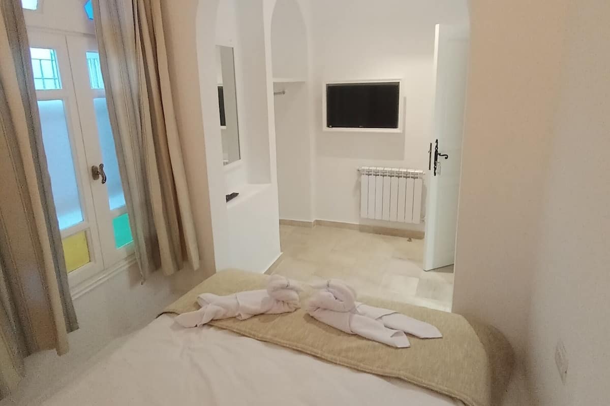 A hotel room with a bed, a TV mounted on the wall, and a bathroom visible through an arched doorway.