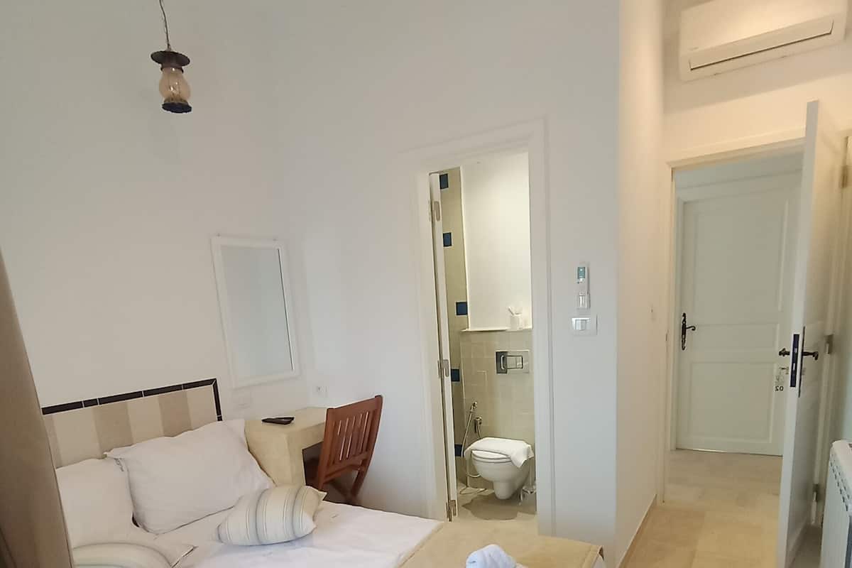 A hotel room with a large bed, a bedside table, a mirror, and a bathroom visible through an open door.