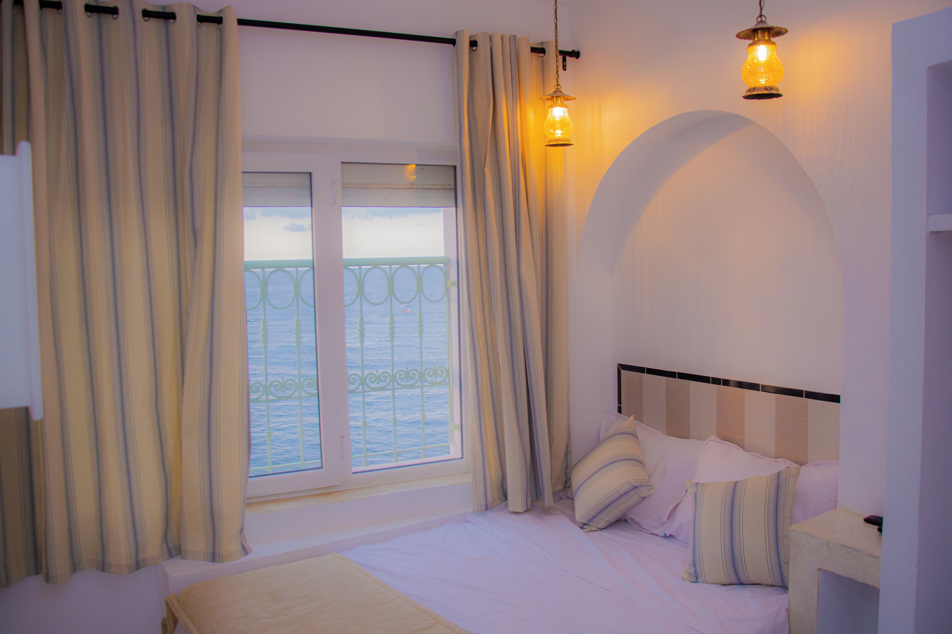 Ein Schlafzimmer mit Bett, Vorhängen, einem Fenster mit Aussicht und einer Wandleuchte.