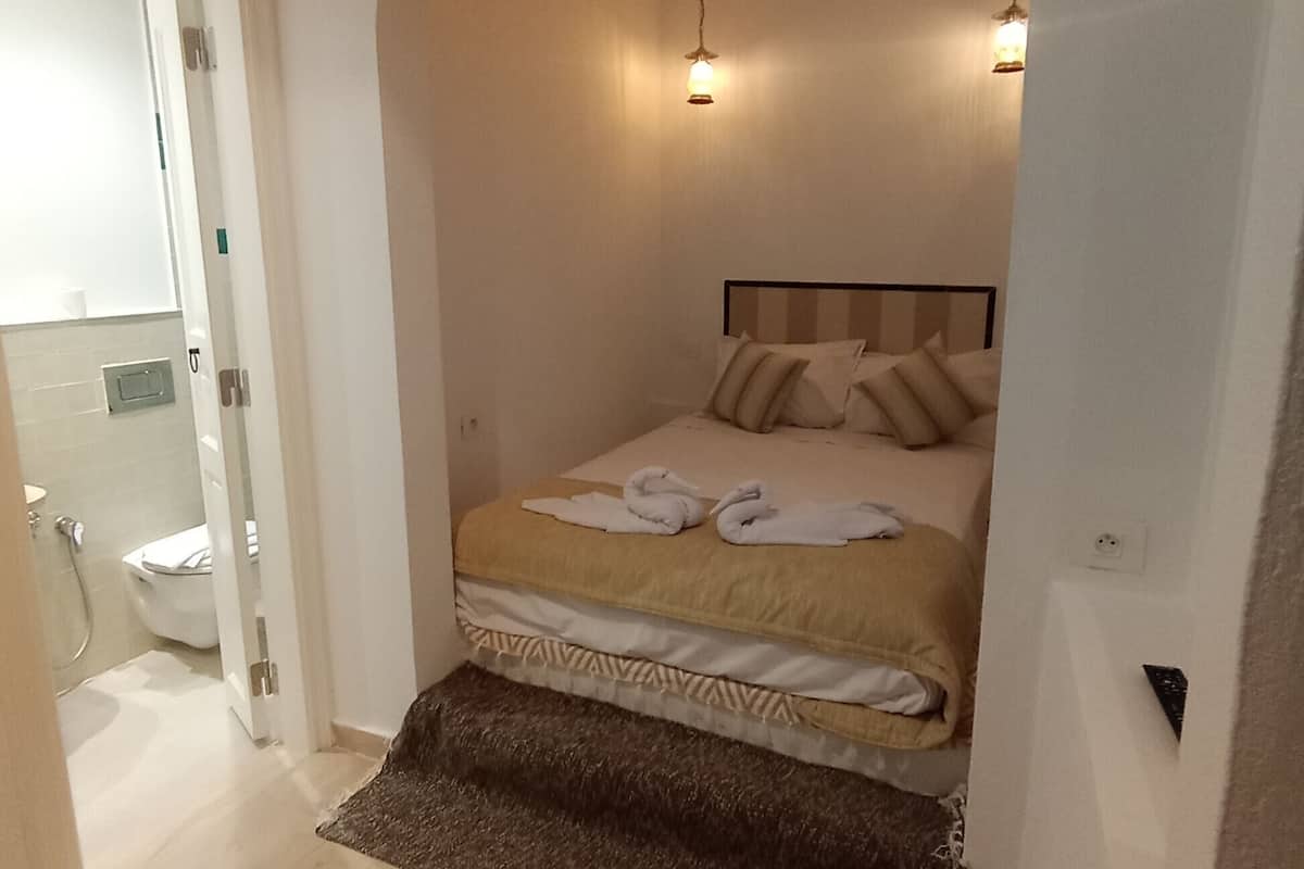 A bedroom with a bed, a small rug, and a bathroom visible through an archway.