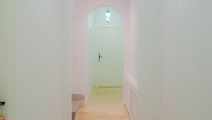 A hallway with a tiled floor, a white door at the end, and a hanging light fixture. - Hotel Al Jazira (Mahdia)