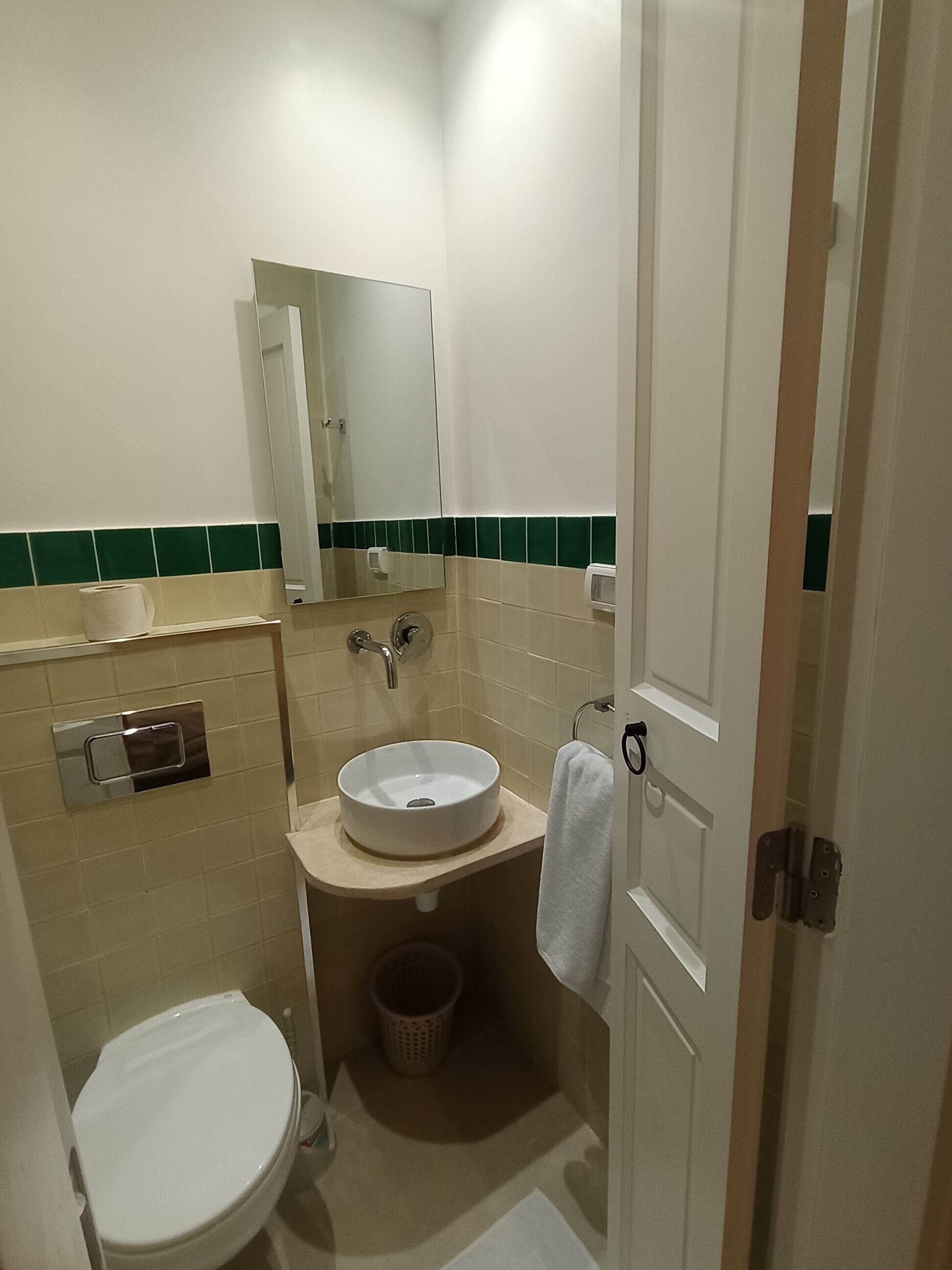 Un baño pequeño con inodoro blanco, lavamanos con espejo y toalla colgada en la puerta.