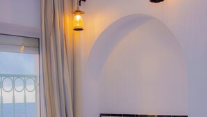 A bedroom with a bed, curtains, a bedside table, and a view of the sea through a window. - Hotel Al Jazira (Mahdia)