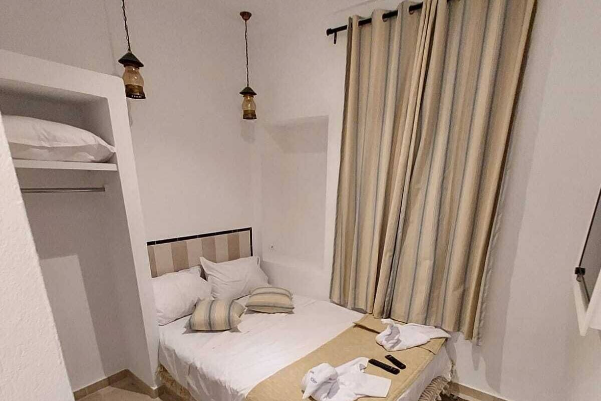 A compact hotel room with a single bed, a small bedside table, a hanging lamp, and a curtain.