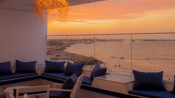 A terrace with seating, a hanging light fixture, and a view of the sea at sunset. - Hotel Al Jazira (Mahdia)