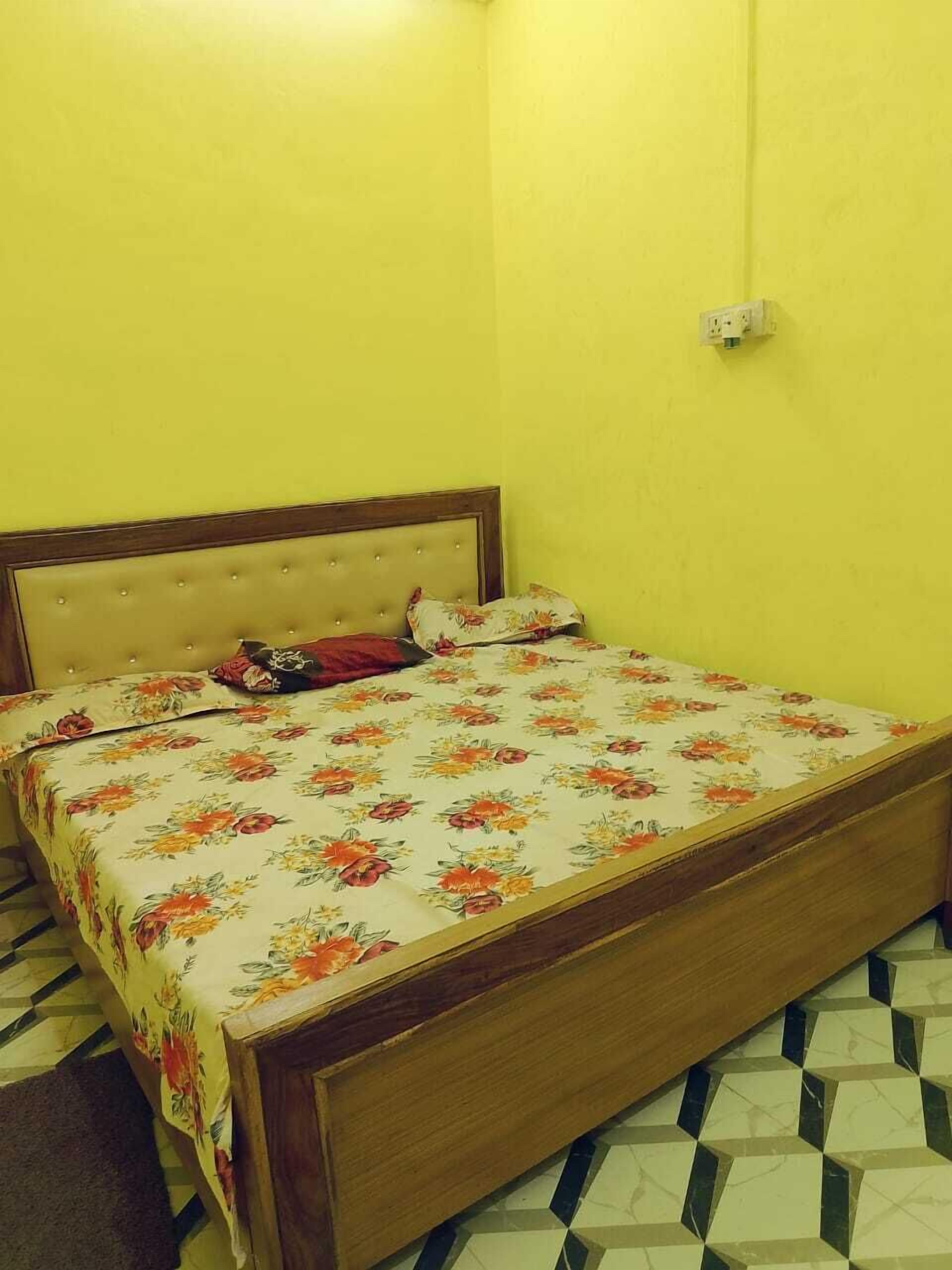 Una cama individual con una colcha estampada y un cabecero de madera en una habitación con paredes amarillas y suelo con diseño.