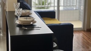 A dining table set with plates, a glass, and cutlery in a room with a view through a window. - Seafront apartment with barbecue on the balcony and swimming pool  (Balneario Umurama Mongaguá)