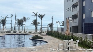 A pool area with lounge chairs and a view of the ocean. - Seafront apartment with barbecue on the balcony and swimming pool  (Balneario Umurama Mongaguá)