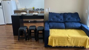 A compact living space with a kitchenette, a dining area, and a sofa with a yellow throw. - Seafront apartment with barbecue on the balcony and swimming pool  (Balneario Umurama Mongaguá)