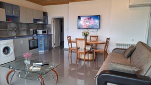 Een moderne keuken met een wasmachine, een eethoek met een glazen tafel, en een zithoek met een bank.