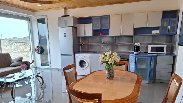 Een moderne keuken met een eethoek, inclusief een glazen tafel en stoelen, een wasmachine en een magnetron.