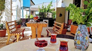 Een ronde tafel met een tafelkleed met patroon, twee houten stoelen, een vaas met bloemen en twee traditionele Turkse theekopjes met een theepot.