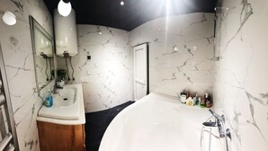 Een moderne badkamer met een marmeren wand, een ruime badkuip, een wastafel en een spiegel.