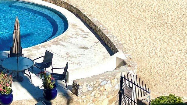 A beach view with a pool area, including a circular pool, lounge chairs, and a table.