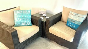 Two wicker armchairs with beige cushions and decorative pillows with beach-themed text.