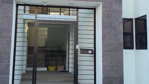 A building entrance with a gated driveway, a visible apartment number, and a balcony with a railing.