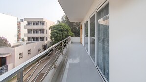 A balcony with a metal railing, a glass door, and a view of adjacent buildings. - Saunter living (Gurugram)